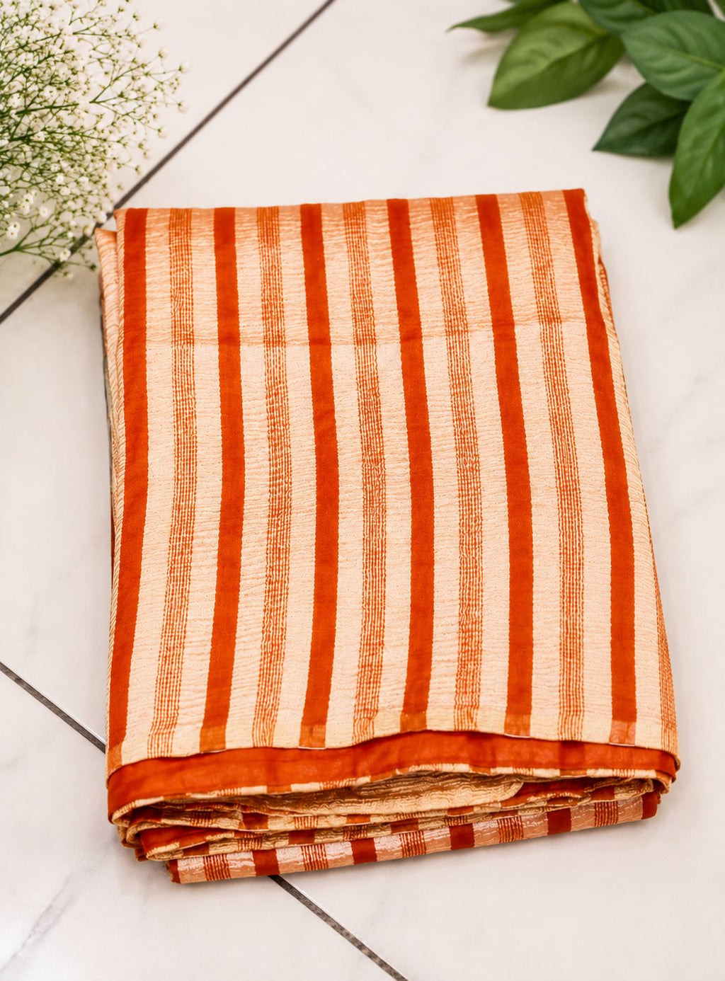 Folded fabric with orange and white stripes on a light wooden surface with green leaves.